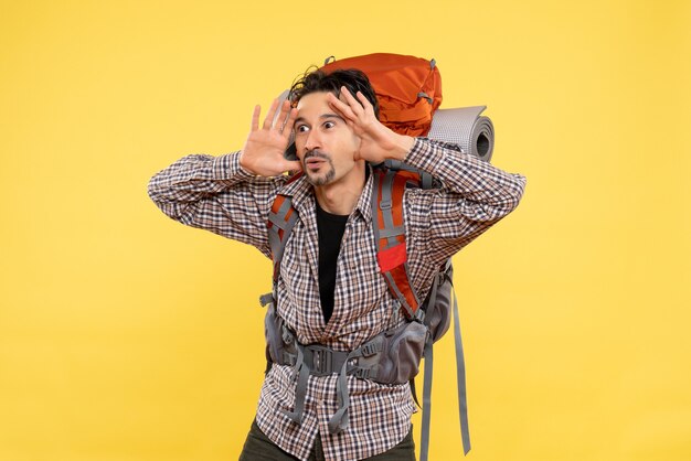 Vista frontal del hombre joven que va de excursión con mochila en el campus de altura humana de montaña turística de color de fondo amarillo