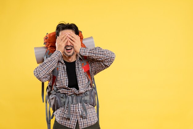 Vista frontal del hombre joven que va de excursión con la mochila que cubre su rostro sobre fondo amarillo viaje de color altura del campus montaña turística humana