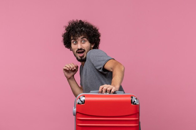 Vista frontal del hombre joven que va de vacaciones con su bolsa roja en el espacio rosa