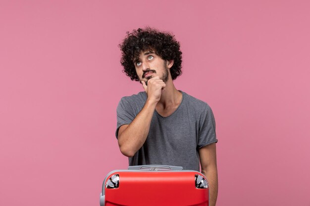 Vista frontal hombre joven que va de vacaciones con su bolso rojo pensando en espacio rosa