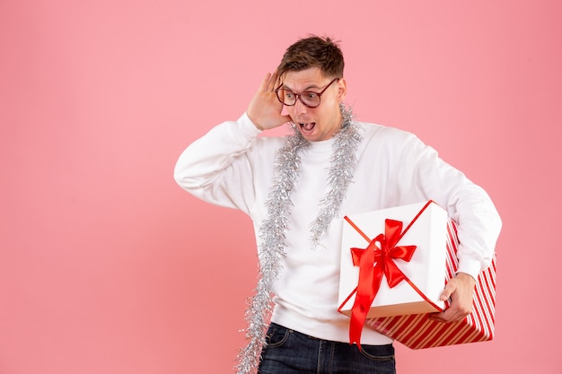 Vista frontal del hombre joven con regalo de Navidad sobre fondo rosa