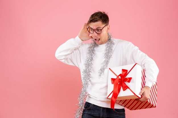 Vista frontal del hombre joven con regalo de Navidad sobre fondo rosa