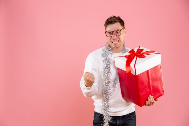 Vista frontal del hombre joven con regalo de Navidad sobre fondo rosa