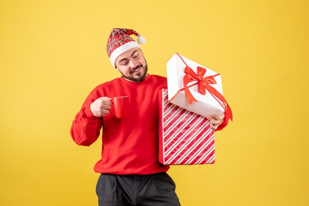 Vista frontal del hombre joven con regalo de Navidad y taza de té sobre fondo amarillo