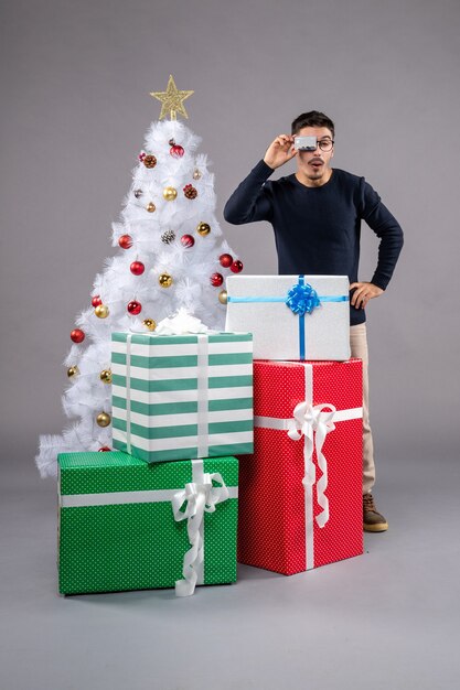 Vista frontal del hombre joven con regalos y tarjeta bancaria en el gris