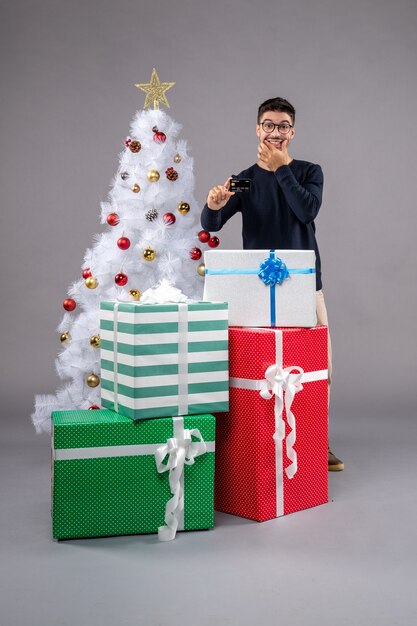 Vista frontal del hombre joven con regalos y tarjeta bancaria en el gris