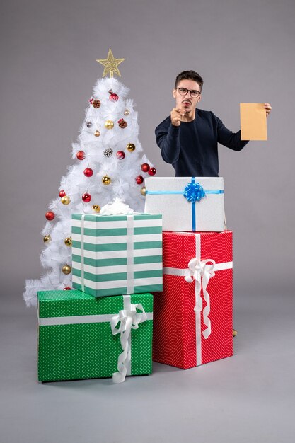 Vista frontal del hombre joven con regalos de vacaciones en el escritorio gris regalo humano de año nuevo de Navidad