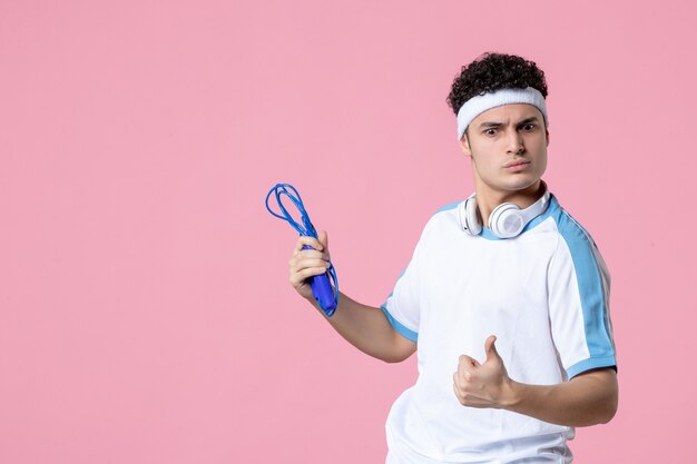 Vista frontal del hombre joven en ropa deportiva con saltar la cuerda en la pared rosa