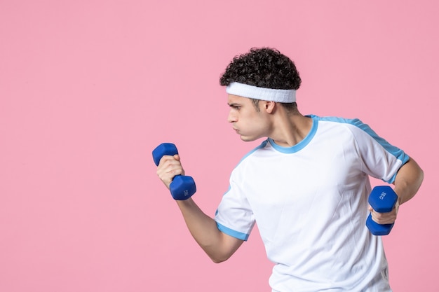 Foto gratuita vista frontal del hombre joven en ropa deportiva trabajando con pesas en la pared rosa