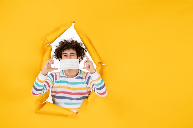 Foto gratuita vista frontal hombre joven sosteniendo la máscara en los colores de la pandemia de la foto humana del coronavirus covid de la salud amarilla