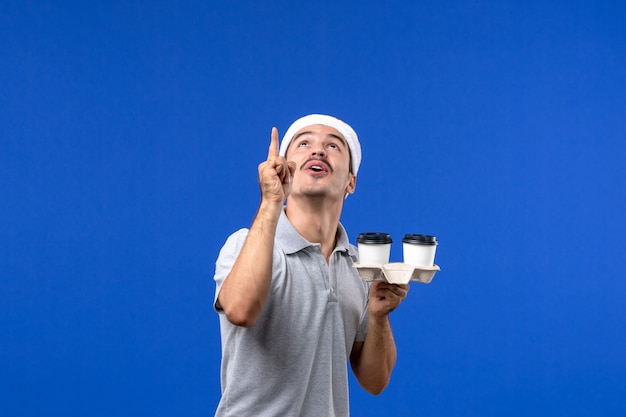 Vista frontal hombre joven sosteniendo tazas de café en la pared azul emoción café azul humano