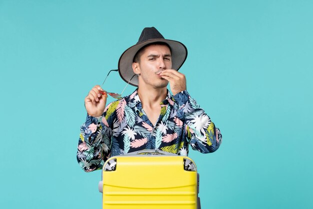 Vista frontal del hombre joven con su bolsa amarilla preparándose para el viaje posando en la pared azul