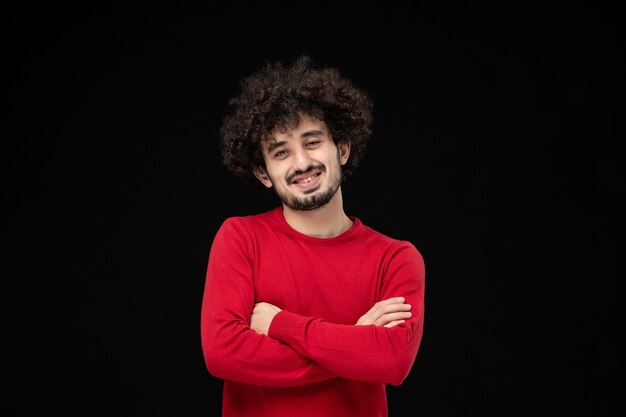 Vista frontal del hombre joven en suéter rojo en la pared negra
