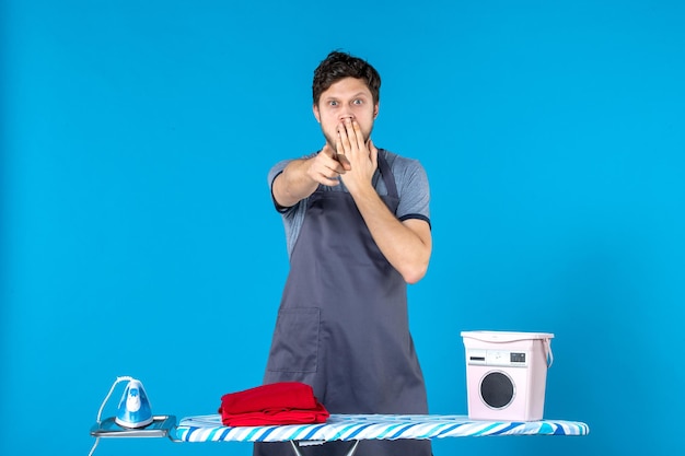 Foto gratuita vista frontal del hombre joven con tabla de planchar conmocionado sobre la superficie azul