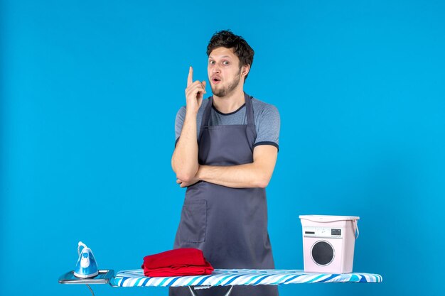 Vista frontal del hombre joven con tabla de planchar sobre fondo azul quehaceres domésticos plancha lavandería lavado hombre limpieza de color