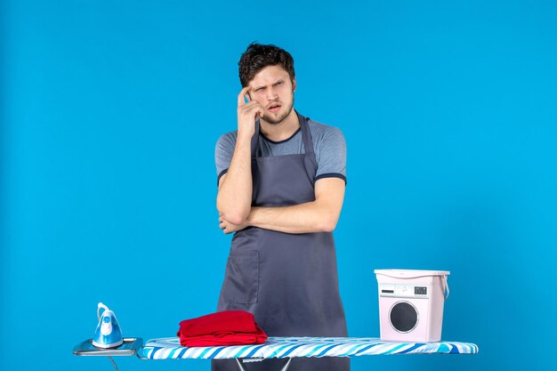 Vista frontal del hombre joven con tabla de planchar sobre fondo azul quehaceres domésticos plancha lavandería lavadora hombre limpieza de color