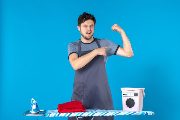 Vista frontal del hombre joven con tabla de planchar sobre la superficie azul