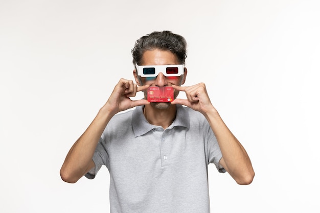 Vista frontal hombre joven con tarjeta bancaria roja en gafas de sol d sobre superficie blanca