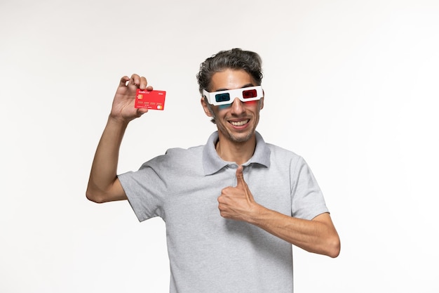 Vista frontal hombre joven con tarjeta bancaria roja en gafas de sol d sonriendo sobre superficie blanca