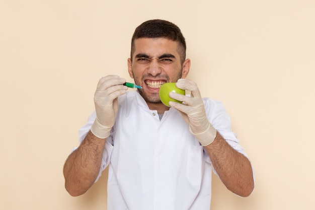 Vista frontal del hombre joven en traje blanco con guantes inyectando manzana en beige