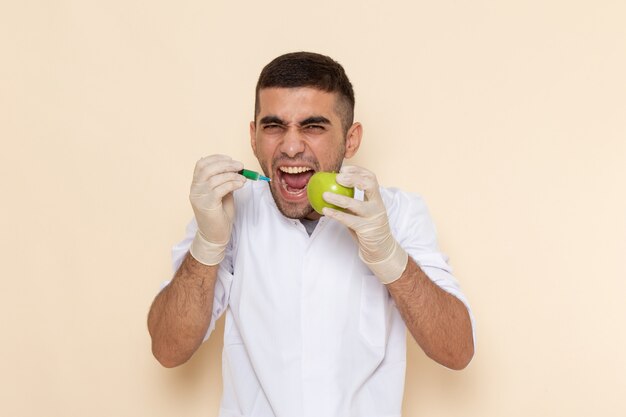 Vista frontal del hombre joven en traje blanco con guantes inyectando manzana gritando en beige