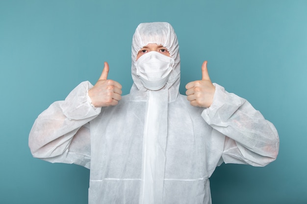 Vista frontal de un hombre joven en traje especial blanco con máscara protectora estéril en la pared azul traje de hombre peligro color de equipo especial