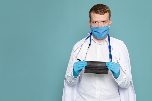 Una vista frontal hombre joven en traje médico blanco y máscara en el espacio azul