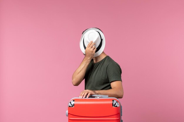 Vista frontal del hombre joven en vacaciones sosteniendo su sombrero en el piso rosa hombre viaje viaje por mar vacaciones vacaciones