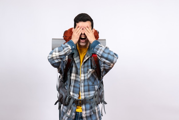 Vista frontal del hombre joven viajero con mochila que cubre los ojos con las manos