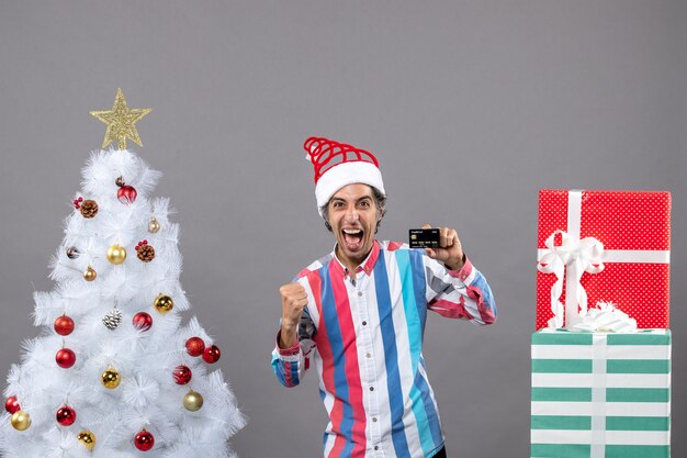 Vista frontal del hombre lleno de alegría en un gesto victorioso de pie cerca del árbol de Navidad blanco