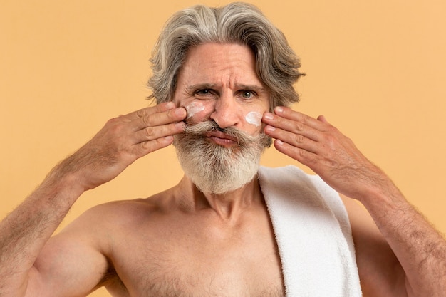 Vista frontal del hombre mayor con barba, aplicar la crema en la cara