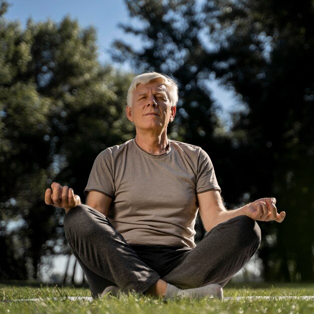 Vista frontal del hombre mayor en posición de loto al aire libre durante el yoga