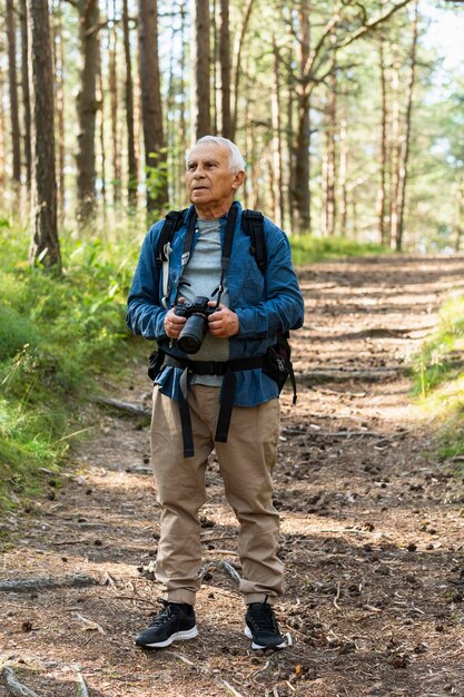 Vista frontal del hombre mayor que viaja con mochila y cámara en la naturaleza