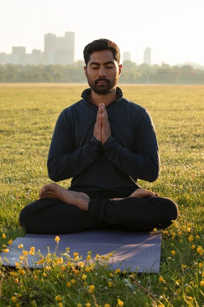 Vista frontal del hombre meditando al aire libre en la estera de yoga