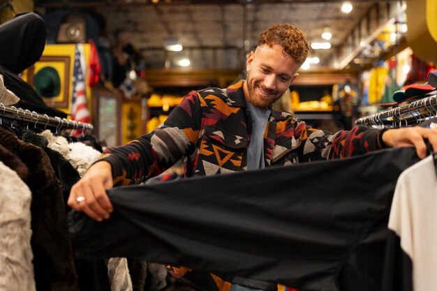 Vista frontal hombre mirando ropa en tienda de segunda mano