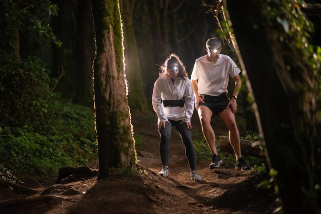 Vista frontal del hombre y la mujer activos caminando en el bosque por la noche. Dos deportistas con ropa deportiva pasando tiempo al aire libre. Ocio, naturaleza, concepto de hobby.