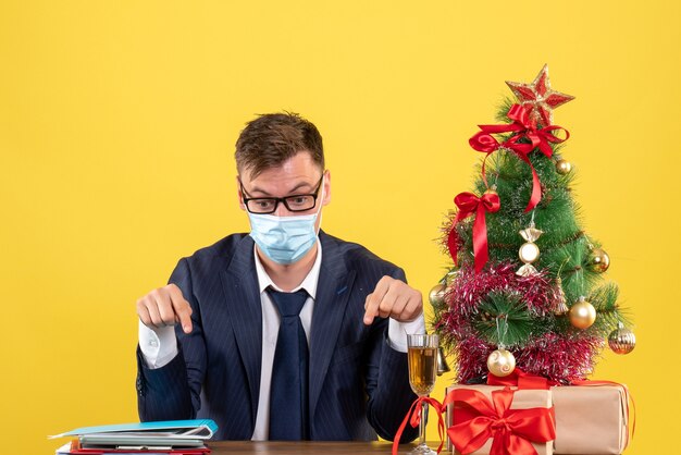 Vista frontal del hombre de negocios apuntando a la mesa árbol de Navidad y presenta en amarillo