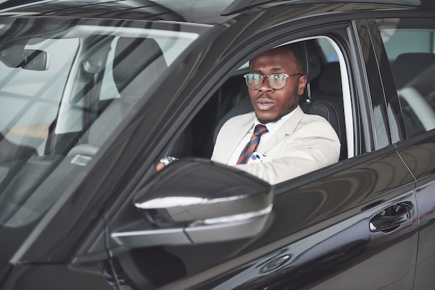 Vista frontal del hombre de negocios serio elegante africano hermoso conduce un coche.