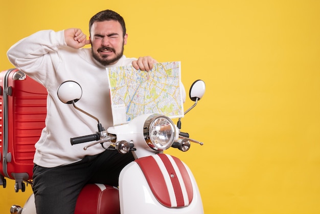 Vista frontal del hombre con problemas sentado en la motocicleta con la maleta en él sosteniendo el mapa que sufre de dolor de oído sobre fondo amarillo aislado