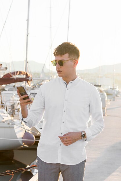 Vista frontal del hombre en el puerto deportivo con smartphone y gafas de sol