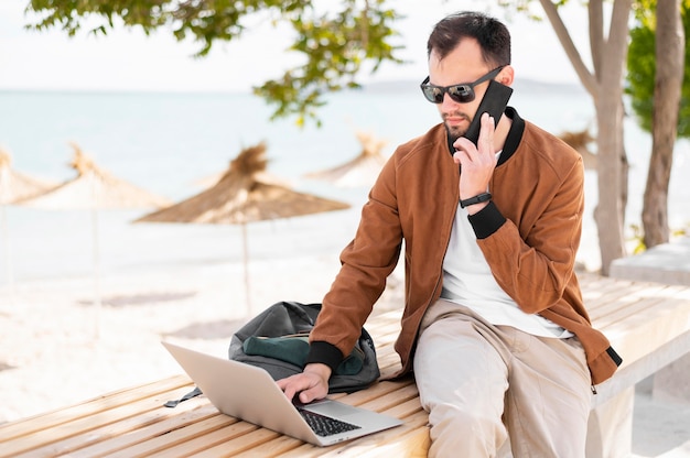 Vista frontal del hombre que trabaja en la computadora portátil en la playa.
