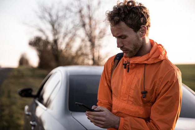 Vista frontal del hombre con smartphone al aire libre durante un viaje por carretera