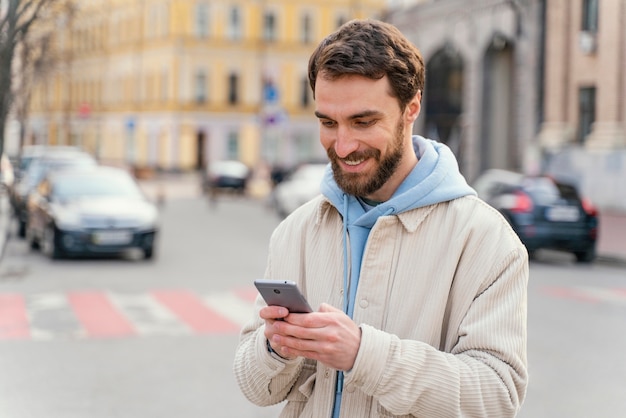 Vista frontal del hombre sonriente al aire libre en la ciudad con smartphone