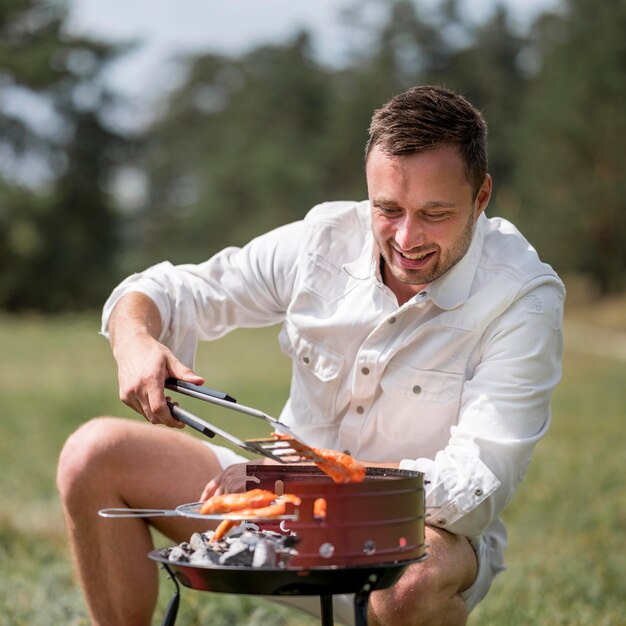 Vista frontal del hombre sonriente asistiendo a la barbacoa al aire libre