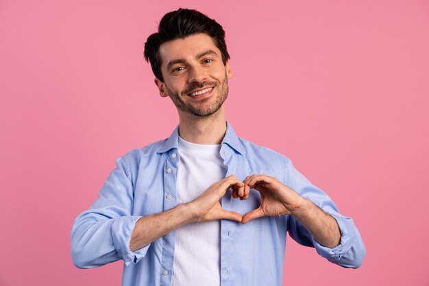 Vista frontal del hombre sonriente haciendo signo de corazón con sus manos