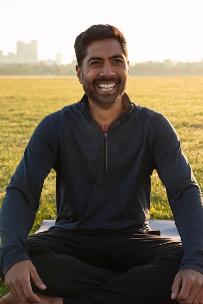 Vista frontal del hombre sonriente meditando al aire libre en la estera de yoga