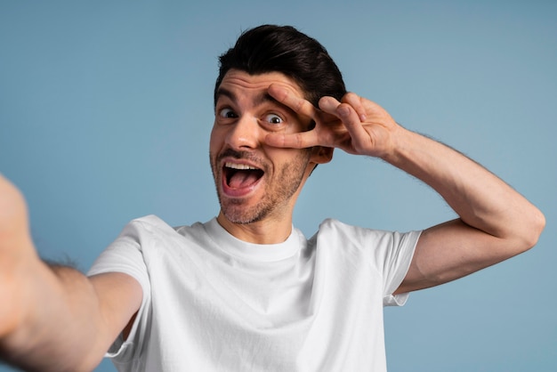 Vista frontal del hombre sonriente tomando un selfie y haciendo el signo de la paz