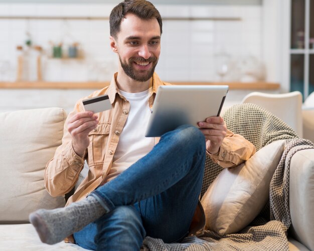 Vista frontal del hombre con tableta y tarjeta de crédito en el sofá