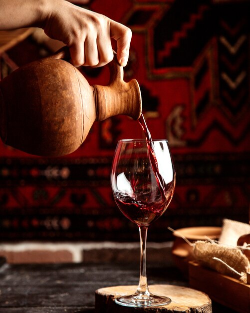 Vista frontal, un hombre vierte de una jarra en una copa de vino tinto