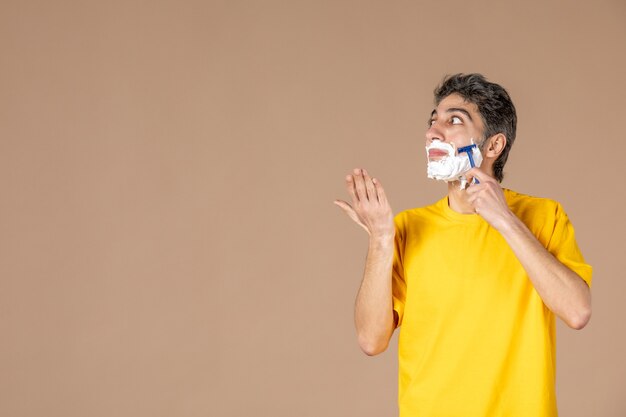 Vista frontal de los hombres jóvenes afeitando su rostro espumoso sobre fondo de color rosa